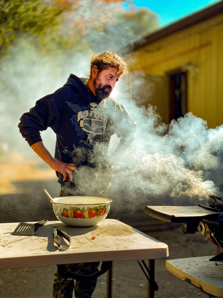 Chef shrouded in smoke while cooking outdoors at a rustic table