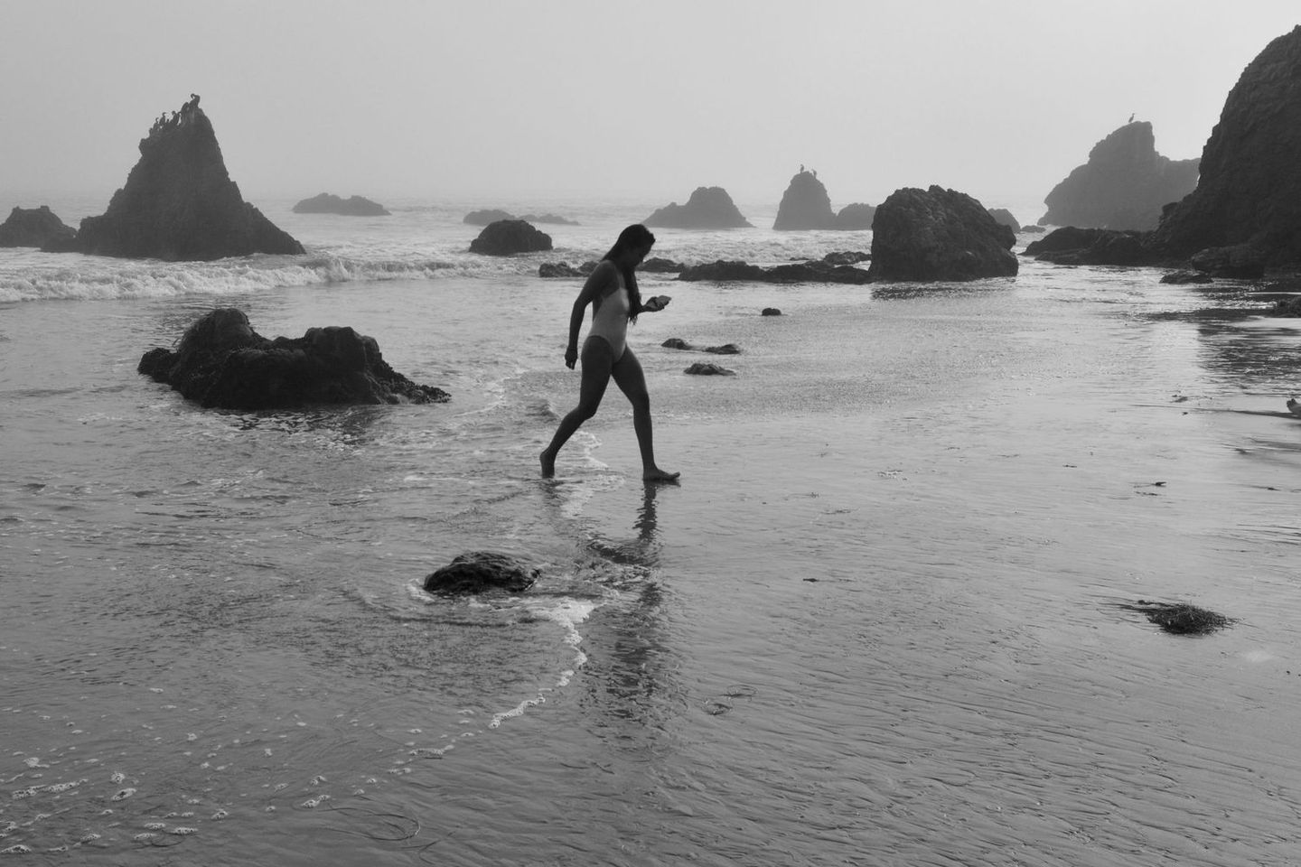 Black and white figure standing among sea rocks