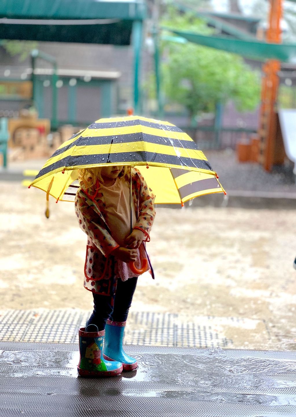 Child under a yellow striped umbrella in the rain