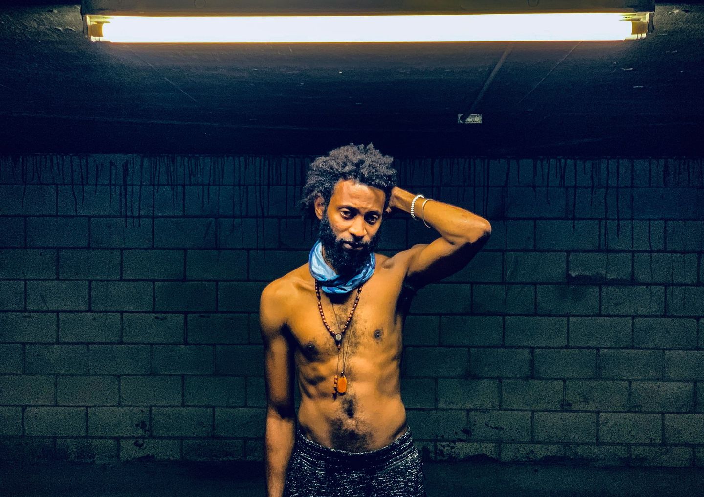 Moody portrait of a shirtless man against a dark blue wall