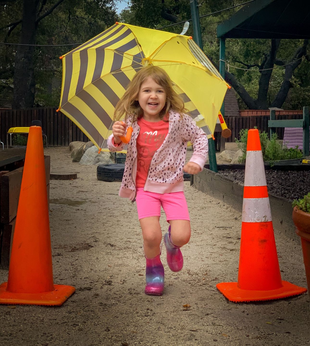 Girl with a yellow striped umbrella skipping between orange traffic cones