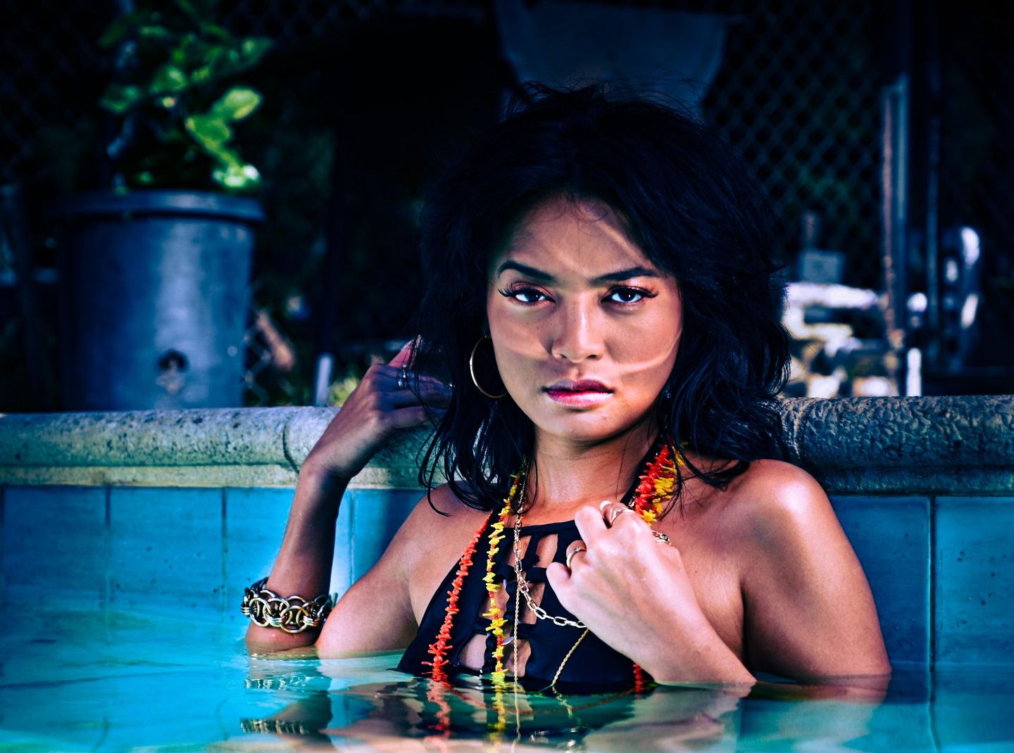 Model in a pool wearing layered red and orange beaded necklaces
