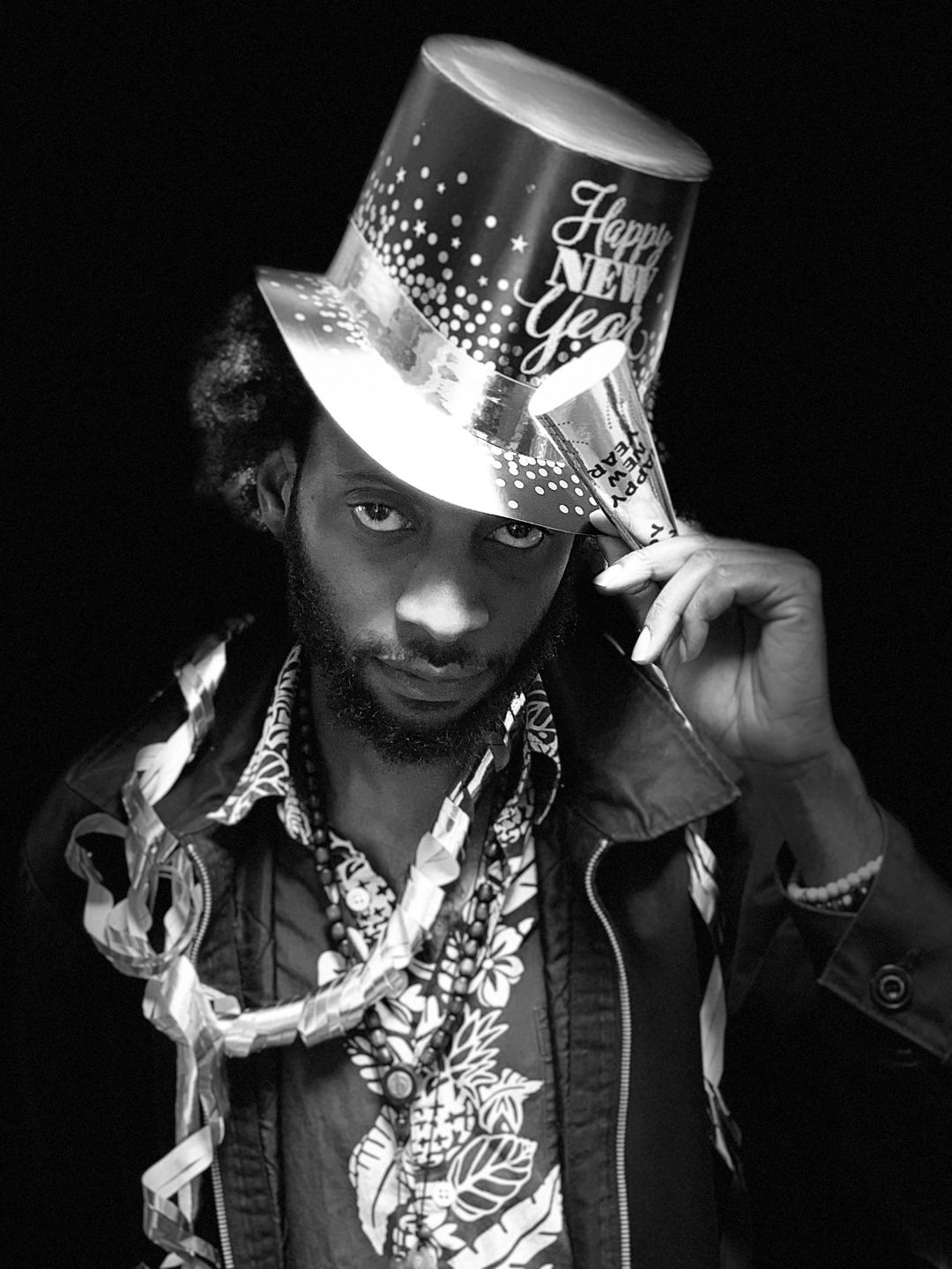 Black and white portrait of a man in a sequined top hat and layered chains