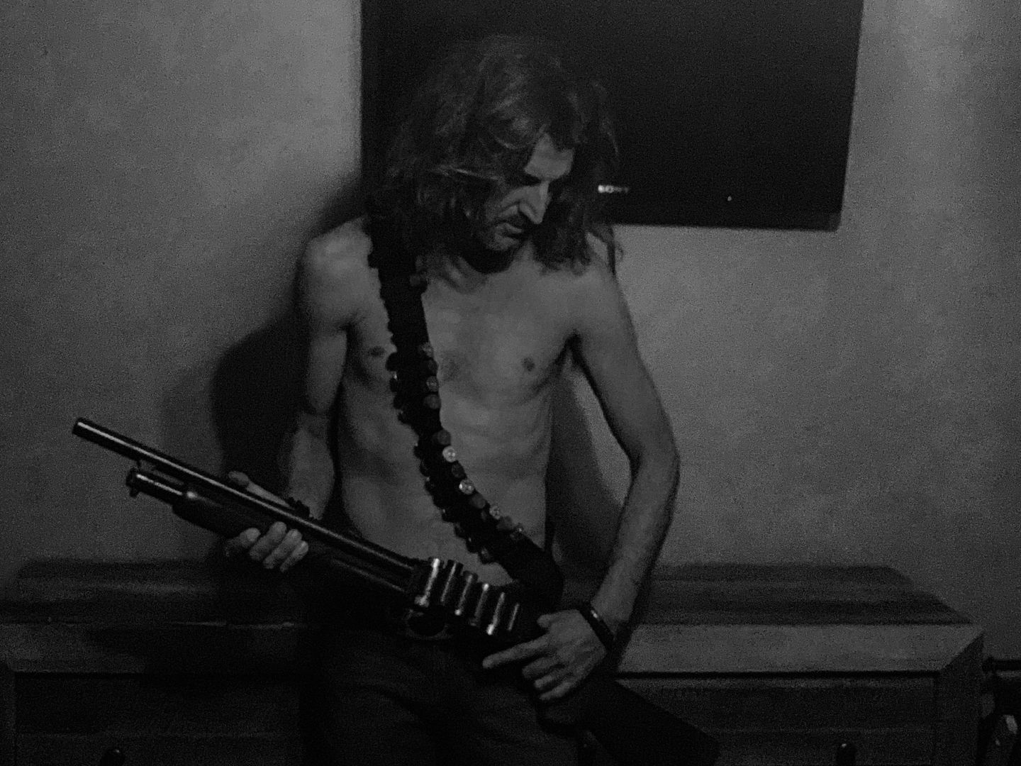 Black and white portrait of a shirtless man holding a rifle with a bandolier