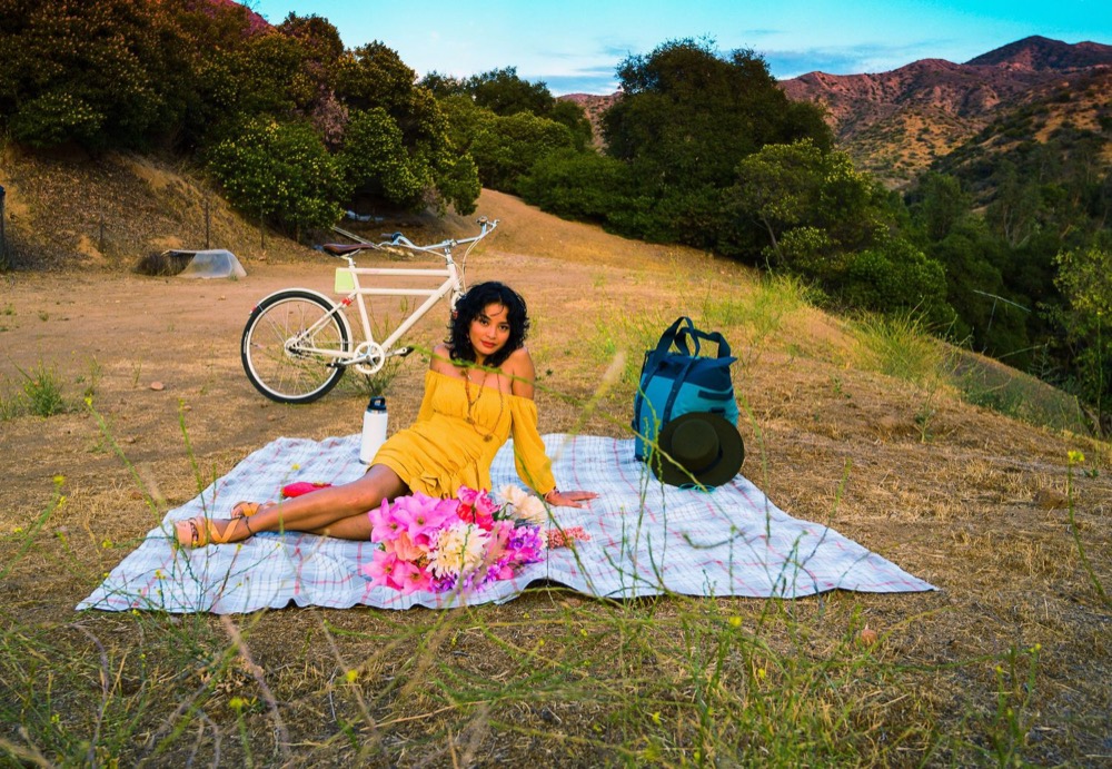 Woman in a yellow top on a picnic blanket in golden hills, bicycle beside her