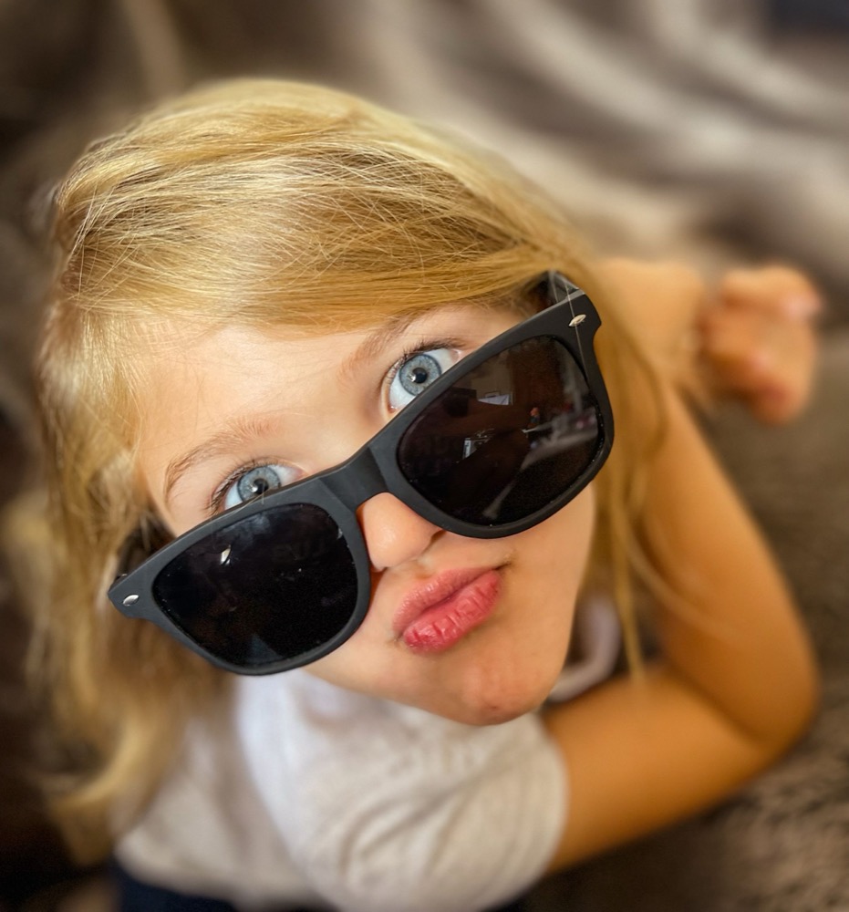 Toddler in oversized sunglasses blowing a kiss